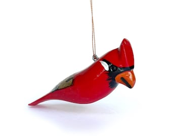 May include: A red cardinal bird ornament with black eyes and a black beak. The ornament is hanging from a brown string.