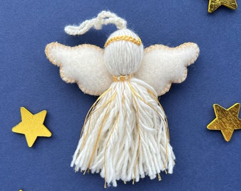 May include: A handmade angel ornament with white yarn hair and a gold halo and accents. The angel has felt wings with gold stitching. Gold star decorations are scattered on a dark blue background.