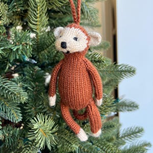 May include: A brown knitted monkey ornament with white face and ears, hanging on a Christmas tree.