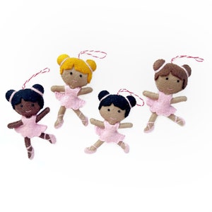 May include: Four felt ballerina ornaments, each with a different hair color and skin tone. The ballerinas are wearing pink tutus and have red string for hanging.