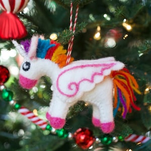 May include: A white felt unicorn ornament with a pink wing, rainbow mane and tail, and black eyes. The ornament is hanging on a Christmas tree.