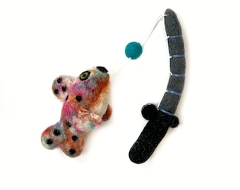 May include: A colorful felt fish toy on a felt fishing rod with a teal ball at the end of the line.