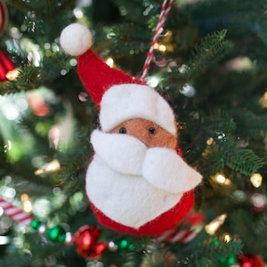 May include: A felt Christmas ornament shaped like Santa Claus. The ornament is red and white with a brown face and black eyes.