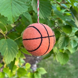 May include: A felt basketball bauble with black stitching, hanging from a red and white string.