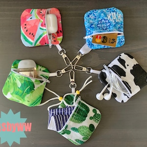 May include: Five different fabric pouches with zipper closures and keychains. Each pouch has a different design: watermelon, tropical leaves, cactus, black and white cow print, and a blue and white geometric pattern. The pouches are all attached to a set of keys with a key ring.