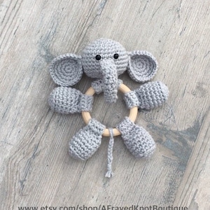 Könnte beinhalten: Ein graues gehäkeltes Elefantenrassel mit einem Holzring. Der Elefant hat einen langen Rüssel und große Ohren.