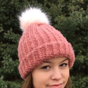 Peut inclure: Un bonnet en tricot rose avec un pompon blanc. Le bonnet est fait d'un fil doux et duveteux.