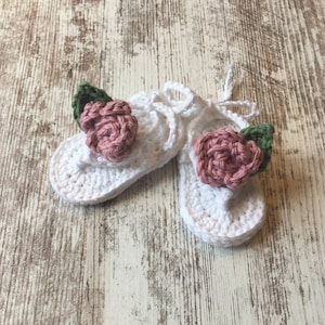 May include: A pair of white crocheted baby sandals with pink and green flower embellishments.