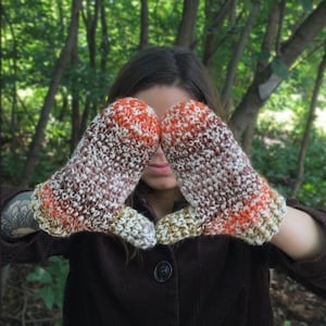 May include: A pair of brown, white, and orange crocheted mittens. The mittens are covering the eyes of a person.