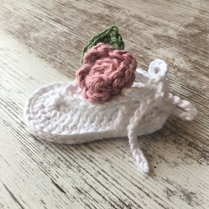 May include: White crocheted baby booties with a pink and green flower embellishment.