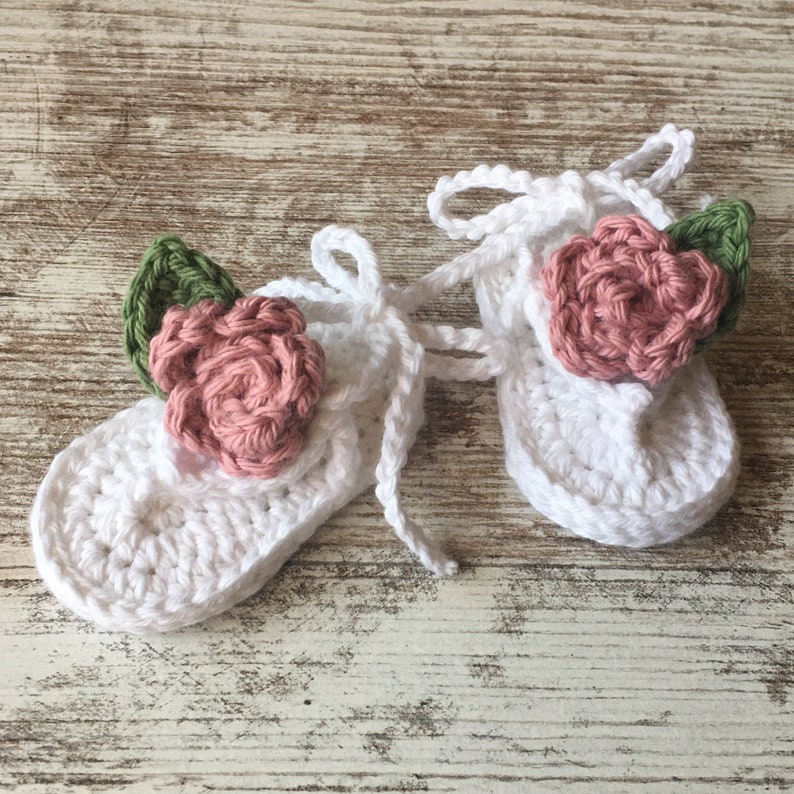 May include: A pair of white crocheted baby shoes with pink and green flower embellishments.