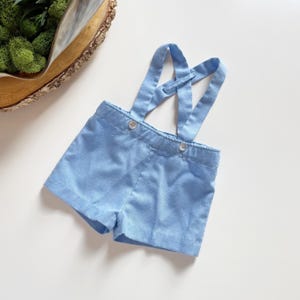 May include: Light blue baby shorts with suspenders. The shorts have a button closure and the suspenders are adjustable.