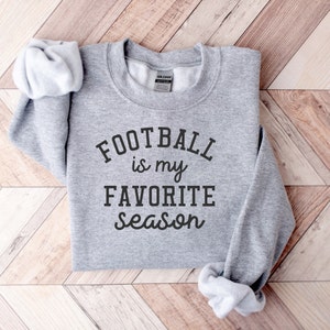 以下が含まれることがあります： グレーのトレーナーに「FOOTBALL is my FAVORITE season」という黒い文字がプリントされています。
