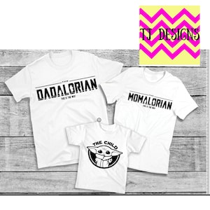 May include: Three white t-shirts with black text. The largest shirt reads "THE DADALORIAN" and "THIS IS THE WAY". The second shirt says "THE MOMALORIAN" and "THIS IS THE WAY". The smallest shirt says "THE CHILD" with a graphic.