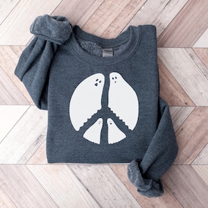 May include: A dark gray sweatshirt with a white peace sign design featuring three ghosts. The ghosts have eyes and mouths.