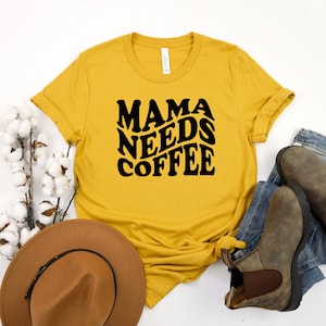 May include: A yellow t-shirt with the text "Mama Needs Coffee" in black retro-style lettering.