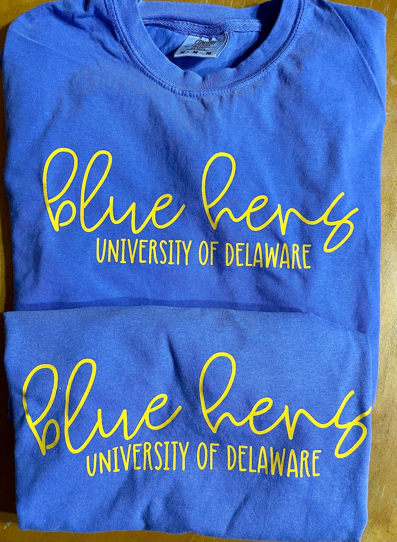 May include: Two blue t-shirts with the words "blue hens" and "University of Delaware" printed in yellow.