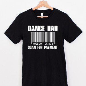 以下が含まれることがあります： 「Dance Dad」とバーコード、そして「Scan for Payment」という白い文字が書かれた黒いTシャツです。