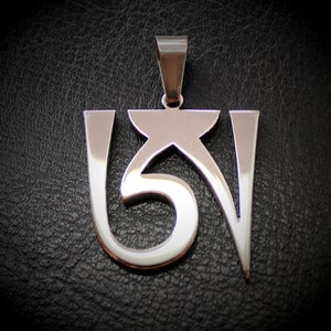 Può includere: Un ciondolo d'argento con un design stilizzato del mantra buddista tibetano Om Mani Padme Hum.