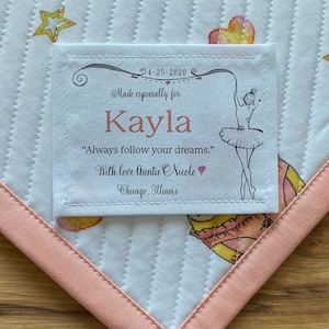 Puede incluir: Una etiqueta de tela blanca con costuras rosas, que presenta una ilustración de bailarina y el texto "4-25-2020 @Made especially for Kayla "Always follow your dreams." With love Auntie Nicole Chicago, Illinois"