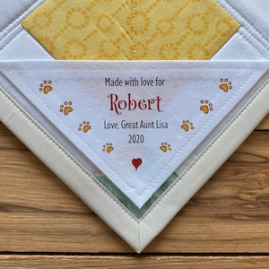 May include: A white triangle-shaped fabric tag with a red heart and paw prints. The tag reads "Made with love for Robert Love, Great Aunt Lisa 2020".