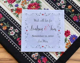 Può includere: Un'etichetta in tessuto bianco con un bordo nero e testo nero che recita "Made with love for Lindsay & Tom November 22, 2020 Love, Mom". L'etichetta è attaccata a una trapunta con un motivo a strisce bianche e nere e disegni floreali.