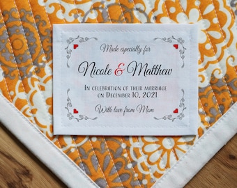 Può includere: Un'etichetta in tessuto bianco con testo nero e cuori rossi. Il testo recita "Made especially for Nicole & Matthew In celebration of their marriage on December 10, 2021 With love from Mom."