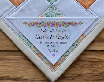 Può includere: Un'etichetta in tessuto triangolare bianca con un motivo floreale e il testo "Made with love for Brooke & Hayden In celebration of their wedding on June 1, 2021 By Mom".