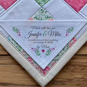 May include: A white triangle-shaped fabric label with green and pink floral designs and the text "Made with love for Jennifer & Miles In celebration of their wedding on October 6, 2020 by Mam".