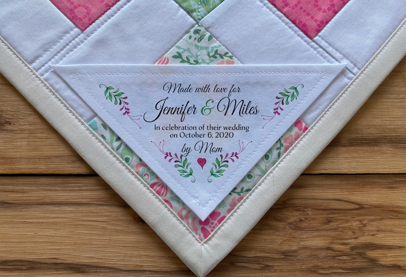 May include: A white triangle-shaped fabric label with green and pink floral designs and the text "Made with love for Jennifer & Miles In celebration of their wedding on October 6, 2020 by Mam".