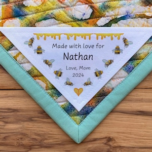 May include: A white triangular tag with a yellow dripping honey design and a border of bees. The tag reads "Made with love for Nathan Love, Mom 2024" with a small yellow heart at the bottom.