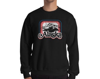 May include: Black sweatshirt with a vintage-style graphic of mountains and the word "Alaska" in a retro font.