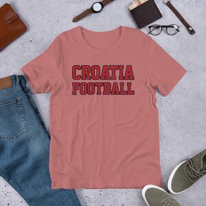 May include: A pink t-shirt with the text "CROATIA FOOTBALL" in red and blue lettering.
