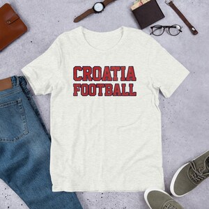 May include: A white t-shirt with a red and blue graphic that says "CROATIA FOOTBALL".