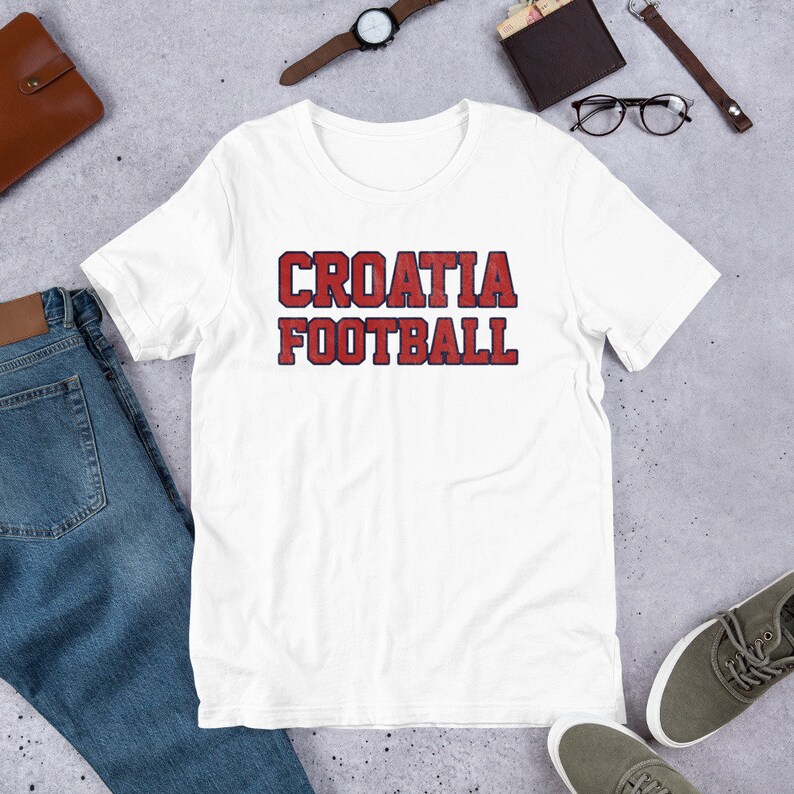 May include: White t-shirt with red and blue text that reads "CROATIA FOOTBALL".
