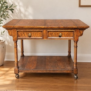 May include: A rectangular wooden side table with a rich brown finish, featuring two drawers with round brass knobs, a lower shelf, and four legs supported by small metal casters. The tabletop has a visible grain pattern and a hinged extension design.