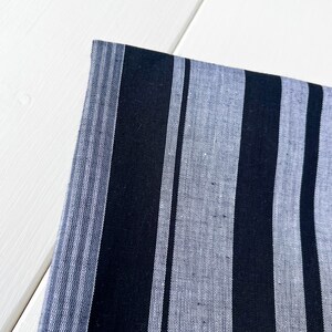 May include: Black and white striped fabric with a subtle texture. The fabric has a woven appearance and is made of a soft, natural material.