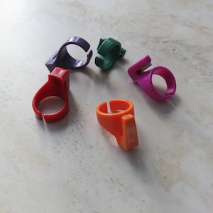 Pode incluir: Cinco cortadores de fio de plástico coloridos, cada um com uma cor diferente: roxo, verde, vermelho, laranja e rosa. Os cortadores são projetados para serem usados em um dedo.