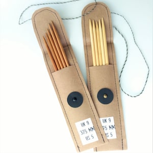 Puede incluir: Dos estuches de papel marrón con costuras negras y cierre de botón negro. Cada estuche contiene un juego de seis agujas de tejer de madera. Los estuches están etiquetados con "UK 9 3.75 MM US 5" y "UK 9 3.75 MM US 5".