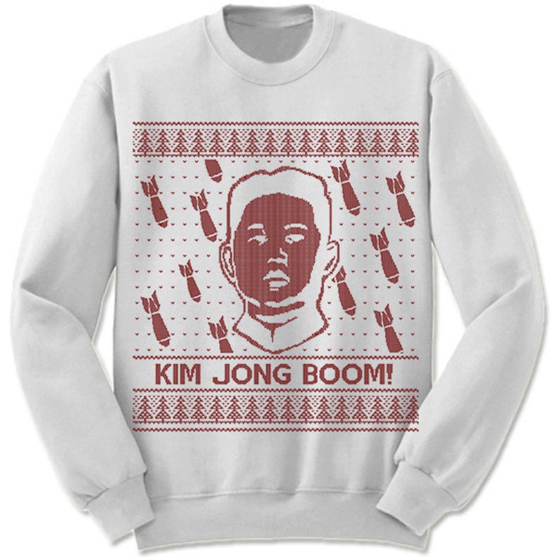 May include: White Christmas sweater with a red knitted design featuring a portrait of Kim Jong-un and the text "KIM JONG BOOM!"