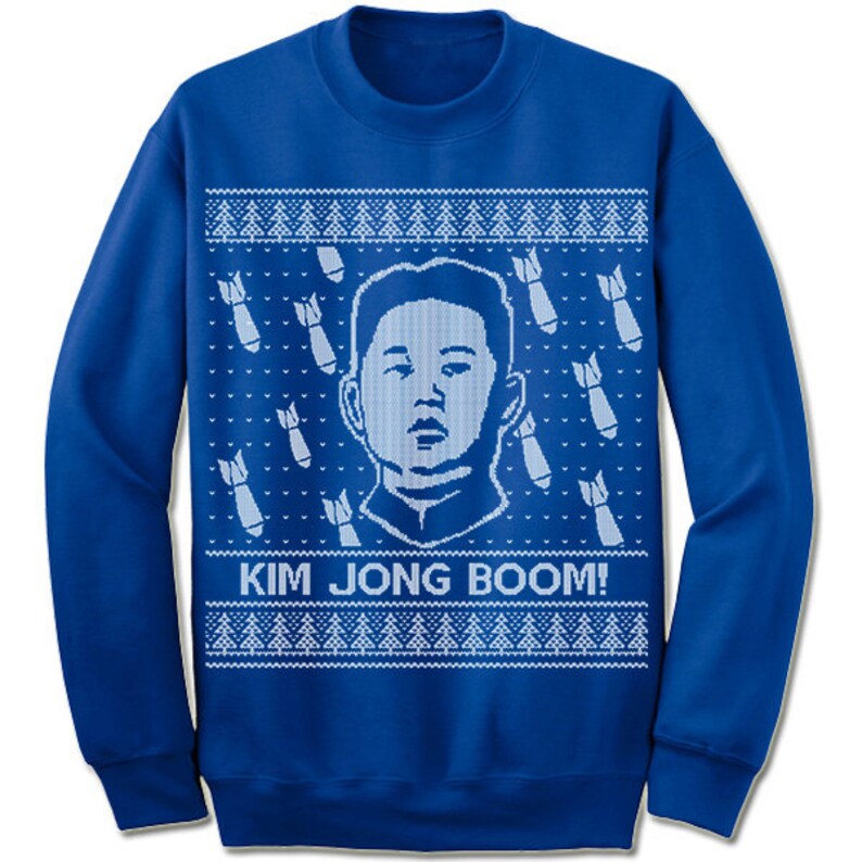 May include: A blue Christmas sweater with a white knit design featuring a cartoon image of Kim Jong-un and the text "KIM JONG BOOM!"