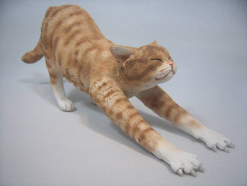 Puede incluir: Una figurita de cer&aacute;mica de un gato jengibre estir&aacute;ndose con las patas extendidas y la cabeza echada hacia atr&aacute;s. El gato tiene patas blancas y un pecho blanco.