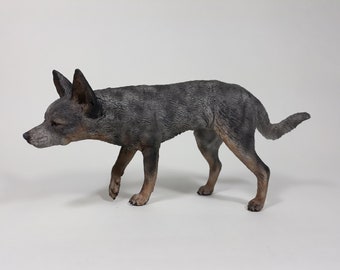 May include: A blue heeler dog figurine, standing on all four legs, with its head tilted down and its tail curled up. The figurine is made of a gray and brown material, and it has a realistic appearance.