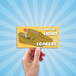 May include: A yellow rectangular sticker featuring a cartoon illustration of two loafers with a lit candle inside one. The text reads "I'M A LITTLE LIGHT IN THE LOAFERS" in white capital letters.