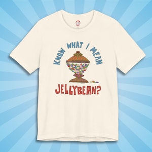 May include: Cream-colored t-shirt with a colorful illustration of a candy jar filled with jellybeans. The text "KNOW WHAT I MEAN JELLYBEAN?" is printed above and below the jar in blue and red.