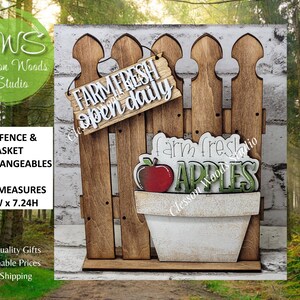 May include: Wooden decorative fence with a sign that reads "FARM FRESH open daily." A white pot with a red apple and the word "APPLES" is attached. The fence measures 5.5"W x 7.24H.