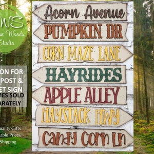 May include: Set of seven wooden signs with arrow shapes and fall-themed text. The signs read: Acorn Avenue, Pumpkin Dr, Corn Maze Lane, Hayrides, Apple Alley, Haystack Hwy, and Candy Corn Ln.