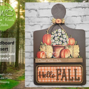 May include: A brown wooden breadboard insert with a fall theme. The insert features a floral arrangement with white flowers, pumpkins, and hay bales. The bottom of the insert has a red and white checkered background with the text "Hello Fall" in brown letters.