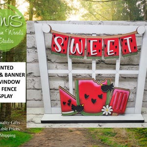 May include: A white wooden window frame display featuring a hanging banner that spells SWEET with watermelon-themed letters. Below, a watermelon slice, a whole watermelon with a bite, and a red popsicle are decorated with black birds.