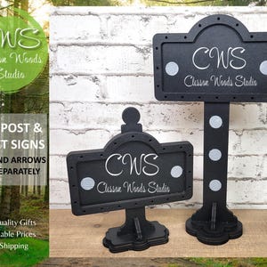 May include: Two black wooden mini post and street signs with white lettering. The signs read "CWS Clesson Woods Studio".